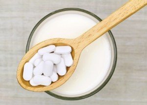 calcium pills in a wooden spoon held above a glass of milk